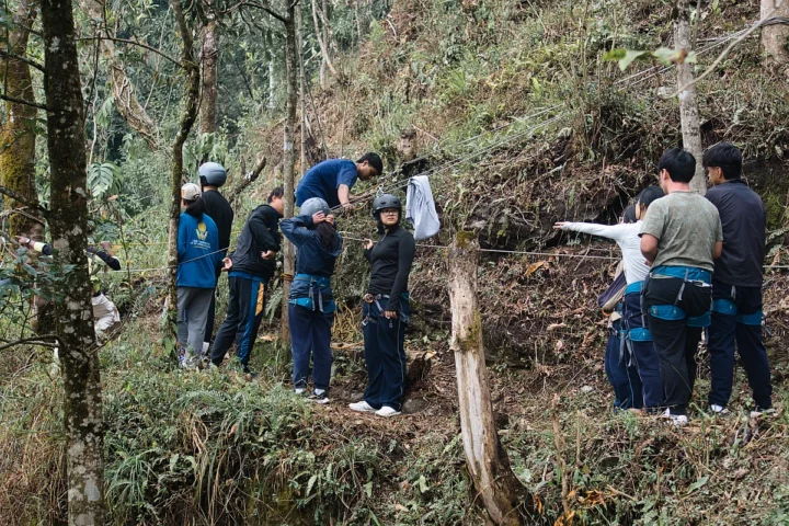 A group of adventure enthusiasts participating in an outdoor rope-based activity in a forested environment in Gangtok-SikkimSome individuals are adjusting their gear, while others are rece
